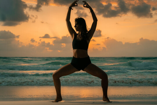 Silhouette of a woman practicing yoga on the beach at sunset in Tulum