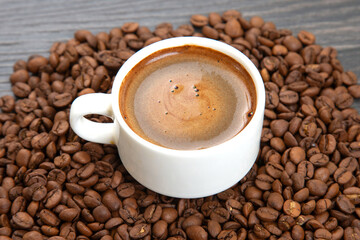 Dark espresso with a velvety crema fills a white cup on a saucer, surrounded by whole coffee beans,...