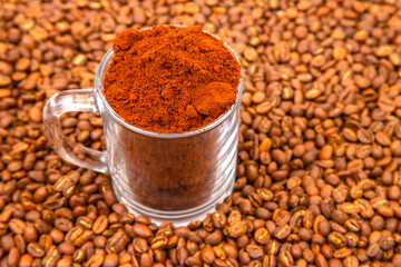 A close-up of a glass mug filled with rich coffee grounds, surrounded by roasted coffee beans,...
