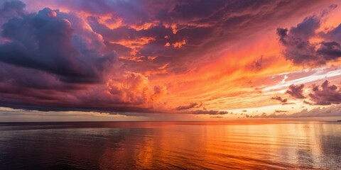 Obraz premium A dramatic sunset over a calm ocean with colorful clouds reflecting in the water