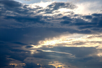 Sunset sky with layered clouds in various shades of blue, gray, and gold. A mesmerizing display of...