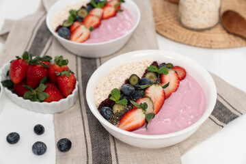 Presented by fruits putting yogurt toppings with strawberry, berry, oats, raisins and chia seed decorated by peppermint in white blow. Pink background. Set of healthy dairy product choice. Pecuniary.