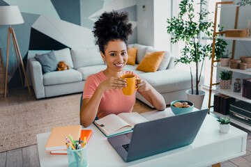 Young woman enjoying a relaxed moment with coffee at home, studying in a bright and cozy living...
