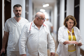 A group of healthcare professionals in white uniforms walking through a hospital hallway while reviewing patient documents and discussing treatment plans.