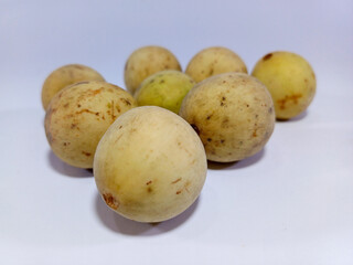 A cluster of perfectly ripe duku fruits, with distinctive light brown, oval-shaped skins, is artfully arranged on a pristine white surface. Their smooth, unblemished surfaces suggest sweet and juicy