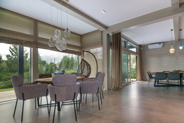 A picturesque summer landscape behind the panoramic windows of the living room with a modern interior design.