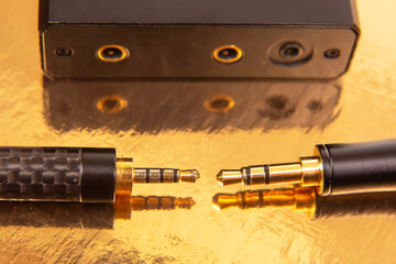 Two 3.5mm headphone jacks with gold-plated tips on a shiny gold background, perfect for showcasing...