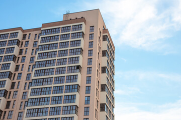 Fototapeta premium A modern high-rise building with a beige facade and large glass windows under a clear blue sky. The architectural design features clean lines and multiple balconies