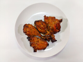 Four pieces of succulent grilled sweet spicy chicken wings are neatly arranged on a clean white...