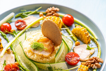 Couscous with chicken pieces, cucumbers, asparagus and corn, tomatoes and walnuts on a blue plate on a light background. Close-up.