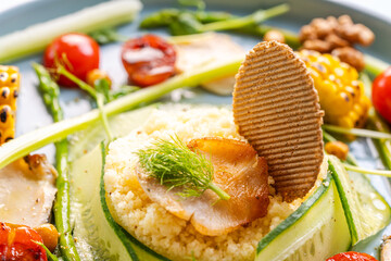 Couscous with chicken pieces, cucumbers, asparagus and corn, tomatoes and walnuts on a blue plate on a light background. Close-up.