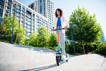 Young woman enjoying summer day on scooter in urban park with smile