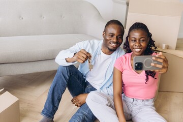 Happy african american couple taking a selfie and showing house keys in their new apartment