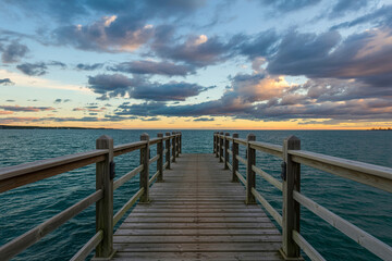 Fototapeta premium Weathered wooden deck leading to a vibrant sunset with dramatic clouds evoking a sense of tranquility and warmth
