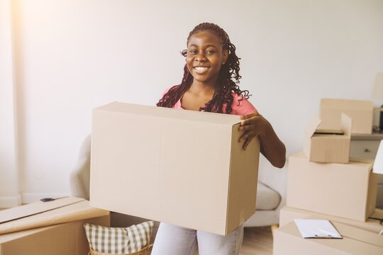 Happy african american woman carrying big cardboard box moving in new house - Powered by Adobe