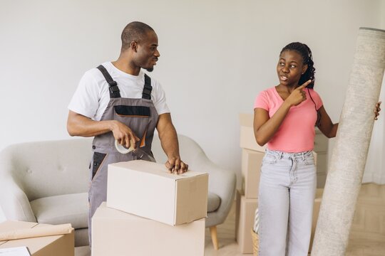 African American Movers Packing Boxes and Carrying Rolled Carpet in New Home