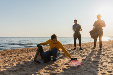 Earth day. Volunteers activists team collects garbage cleaning of beach coastal zone. Woman mans...