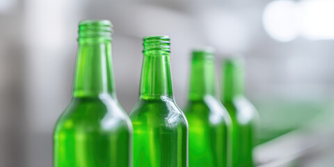 Green glass bottles are aligned in a row on a blurred conveyor belt. Industrial production, glass manufacturing