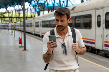Young man using mobile phone app for train ticket, hotel booking, searching location map or reading...