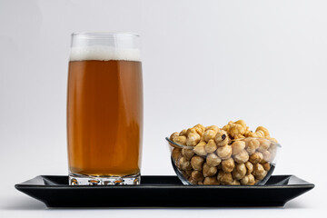 Glass of beer with roasted chickpeas on a black tray over white background