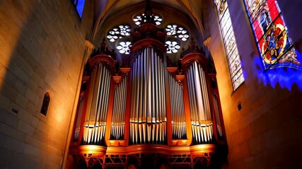 Impressive pipe organ in an old church, arched ceiling, intricate stained glass windows, and stone walls bathed in warm and cool ambient light. - Powered by Adobe