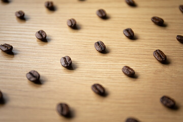 A collection of individual coffee beans is scattered over a wooden background, illuminated softly to emphasize texture and detail