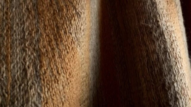 Cozy warm woolen blanket with tassels hanging on rustic wooden wall, brown and gray toned, soft texture for interior design and winter vibes