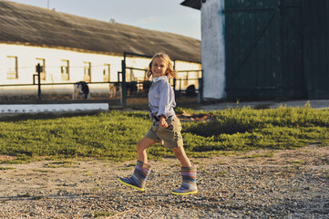 Horizontal photo of smiling farmer kid walking on a farm in summer. Happy childhood in the countryside. Copy space for text