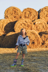 Portrait of kid girl on the farm posing near rolls of hay bales, summertime in countryside, childhood and dreams