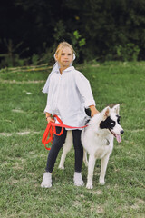 Vertical shot of a little blond girl hugging her pet dog outdooors on nature in summer.  Yakutian Laika dog breed. Happy summertime