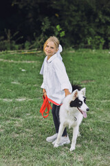 Little blond girl in white shirt walking with her pet dog outdooors on nature in summer. Yakutian Laika dog breed. Happy childhood