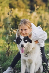 Little blond girl in white shirt with her pet dog outdooors on nature in summer. Yakutian Laika dog breed. Happy childhood concep