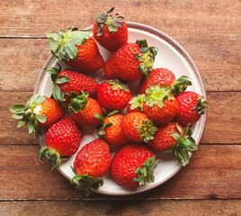 fresh strawberries on porcelain plate and wooden background seen from above