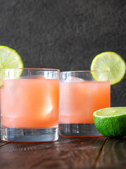 Two guava margaritas with lime wheels glow against rich dark cocktail backdrop