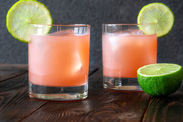 Two guava margaritas with lime wheels glow against rich dark cocktail backdrop