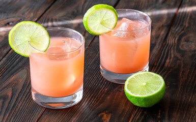 Two guava margaritas with lime wheels glow against rich dark cocktail backdrop