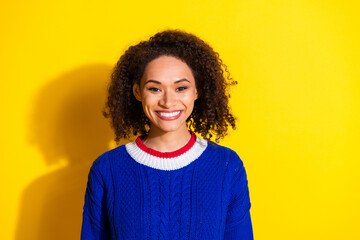 Smiling young woman with curly hair in a blue sweater against a vibrant yellow background