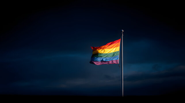 A vibrant rainbow pride flag waving proudly against a dark and moody blue sky background scene outdoors