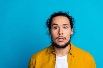 Fototapeta premium Surprised young man in a yellow shirt looking astonished against a vibrant blue background