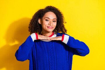 Young woman posing cheerfully against a vibrant yellow backdrop wearing a trendy blue sweater