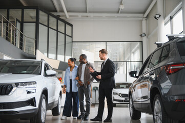 Car salesman showing new car to african american couple in dealership