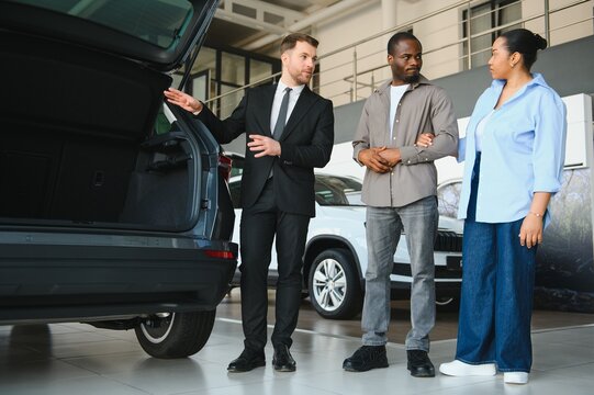Car salesman showing trunk to african american couple in dealership