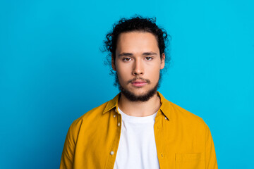 Portrait of a confident young man posing on a vibrant blue background wearing a yellow shirt and maintaining a relaxed expression