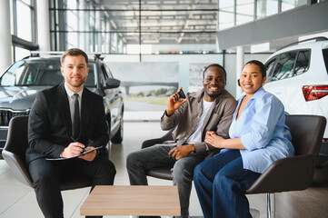 Happy couple holding new car keys with salesman in dealership