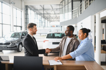 Couple shaking hands with car salesman in dealership