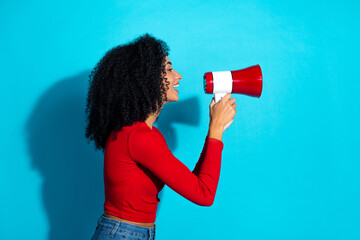Attractive young woman enthusiastically speaking through a megaphone against a vibrant blue...