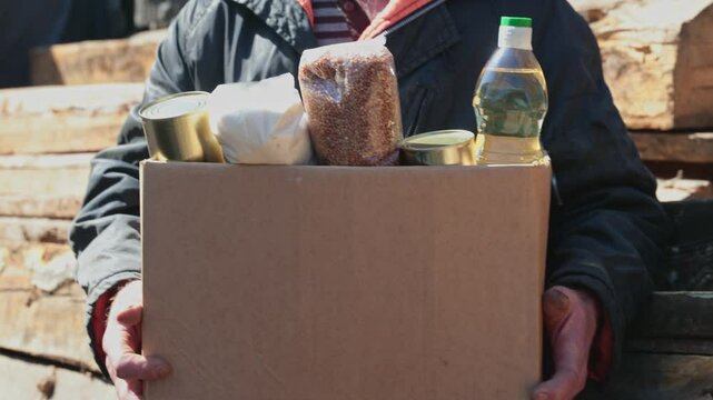Concept humanitarian aid community charity donations center with sunlight. Homeless refugee is holding box food.