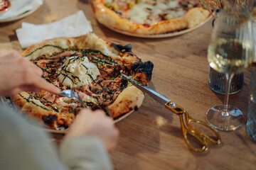 Woman cutting gourmet pizza with burrata and pistachios at restaurant table