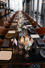Panoramic view of an elegant black table setting with white roses, glasses, napkins, and black plates. Perspective leads into the distance. Refined and minimal atmosphere of a sophisticated event.
