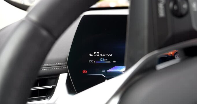 Fast charging session shown on digital dashboard as an electric vehicle charges at 122 kW DC, reaching 50 percent at 15:54 in a modern interior with motion elements